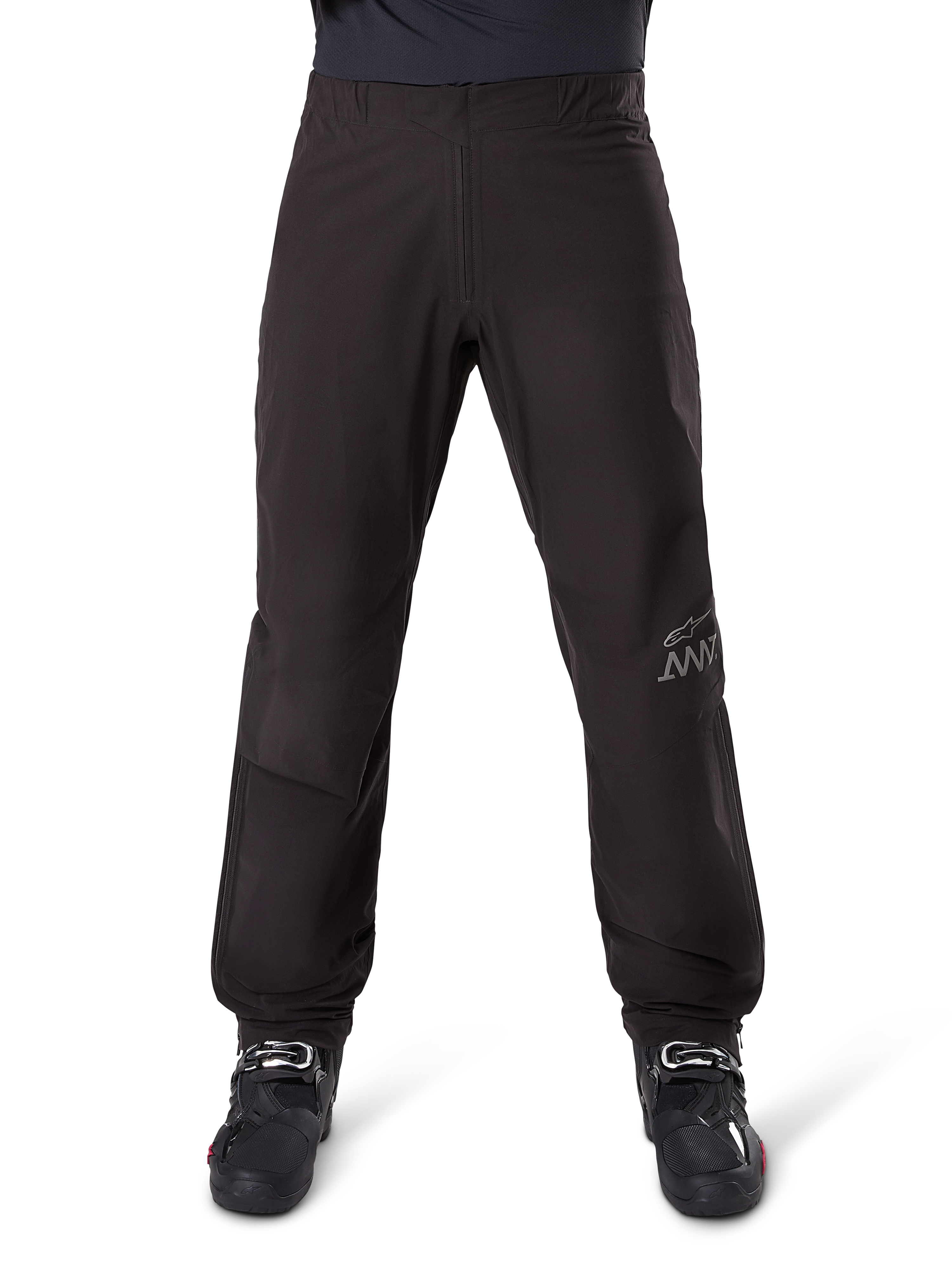 Alpinestars AMT-8 Stretch Drystar® XF bukseliner, sort, set forfra båret med sorte motorcykelstøvler, med gråt stjernelogo og AMT-branding på benet, alsidigt vandtæt og vindtæt motorcykeltøj