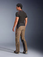 Alpinestars AMT-8 Stretch Drystar® XF bukser i Walnut Black, adventure-touring motorcykelbukser vist skråt bagfra, med nøddebrunt tekstil og sorte paneler på sædet og indersiden af benene, harmonika-strækpaneler på læggene og AMT-branding på siden, båret med et sort baselayer.