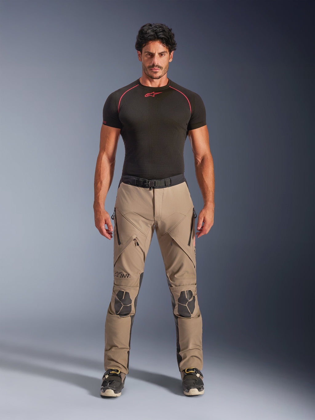 Mandlig model iført Alpinestars AMT-8 Stretch Drystar® XF bukser i Walnut og sort, kombineret med et sort kortærmet basislag, adventure touring-bukser med forstærkede knæ, lynlåslukket ventilation og ergonomisk strækdesign.