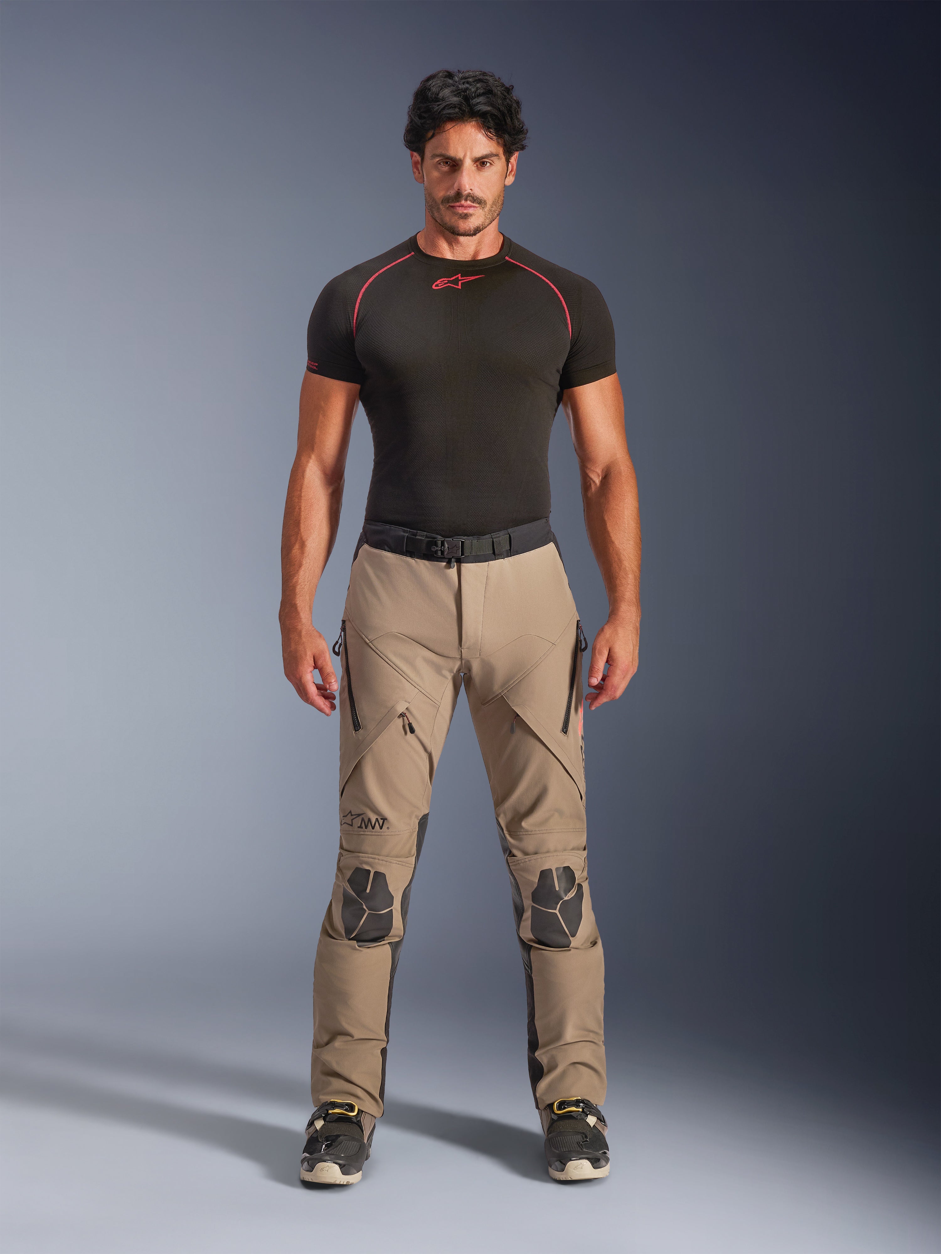 Mandlig model iført Alpinestars AMT-8 Stretch Drystar® XF bukser i Walnut og sort, kombineret med et sort kortærmet basislag, adventure touring-bukser med forstærkede knæ, lynlåslukket ventilation og ergonomisk strækdesign.
