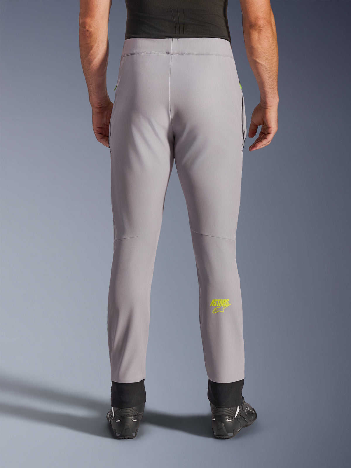 Alpinestars Aeroshell bukser, motorcykelbukser, mellemgrå og Yellow Fluo, set bagfra med gult Astars-logo på læggen, sorte elastiske ankelmanchetter, moderne softshell tekstildesign til landevejs- og fritidskørsel