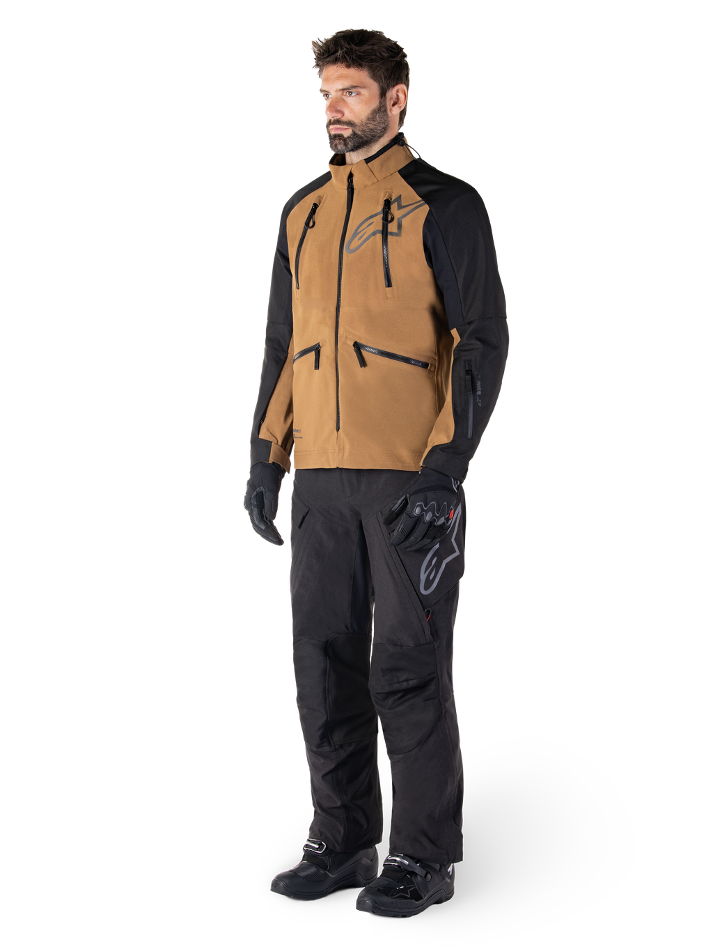 Alpinestars Hyde XT Drystar® bukser, adventure-motorcykelbukser, sort, båret med en brun og sort teknisk jakke, sorte handsker og støvler, med et over-the-boot-design til off-road- og dual-sport-kørsel