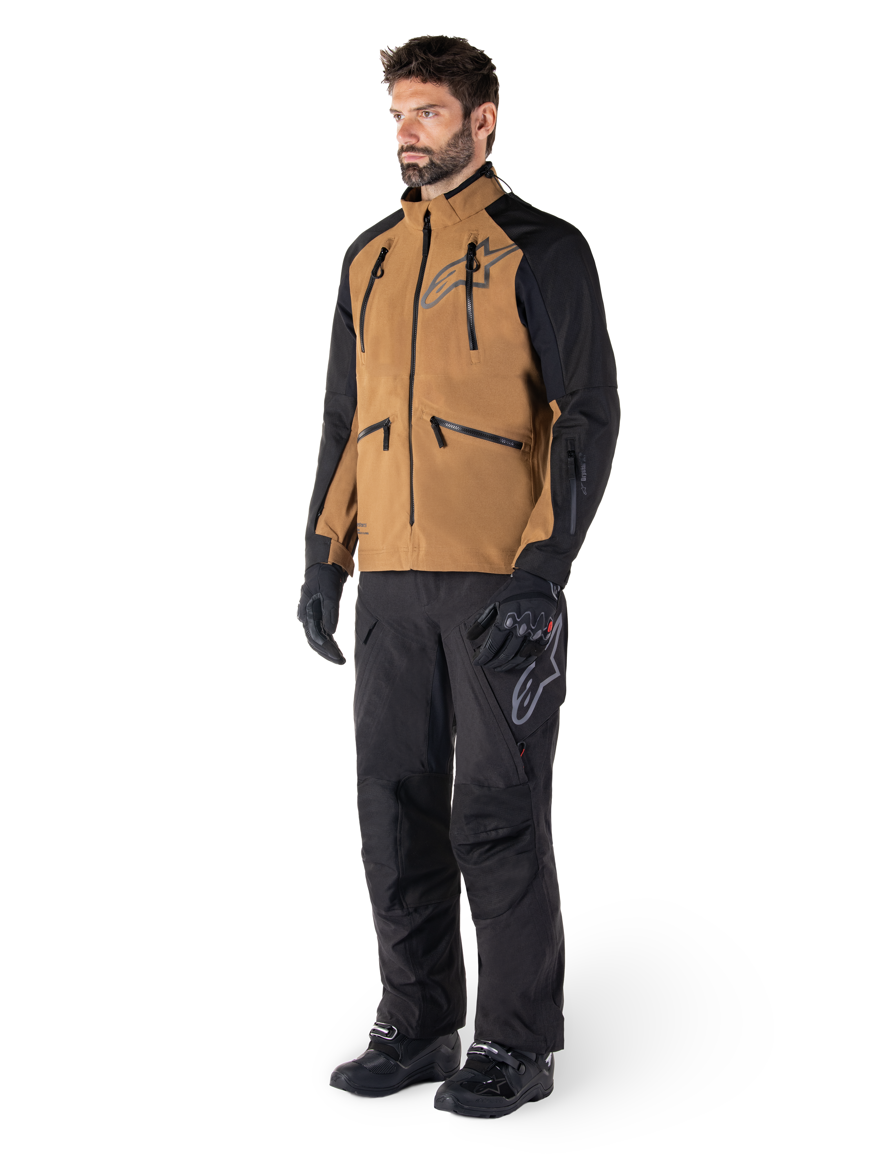 Alpinestars Hyde XT Drystar® bukser, adventure-motorcykelbukser, sort, båret med en brun og sort teknisk jakke, sorte handsker og støvler, med et over-the-boot-design til off-road- og dual-sport-kørsel
