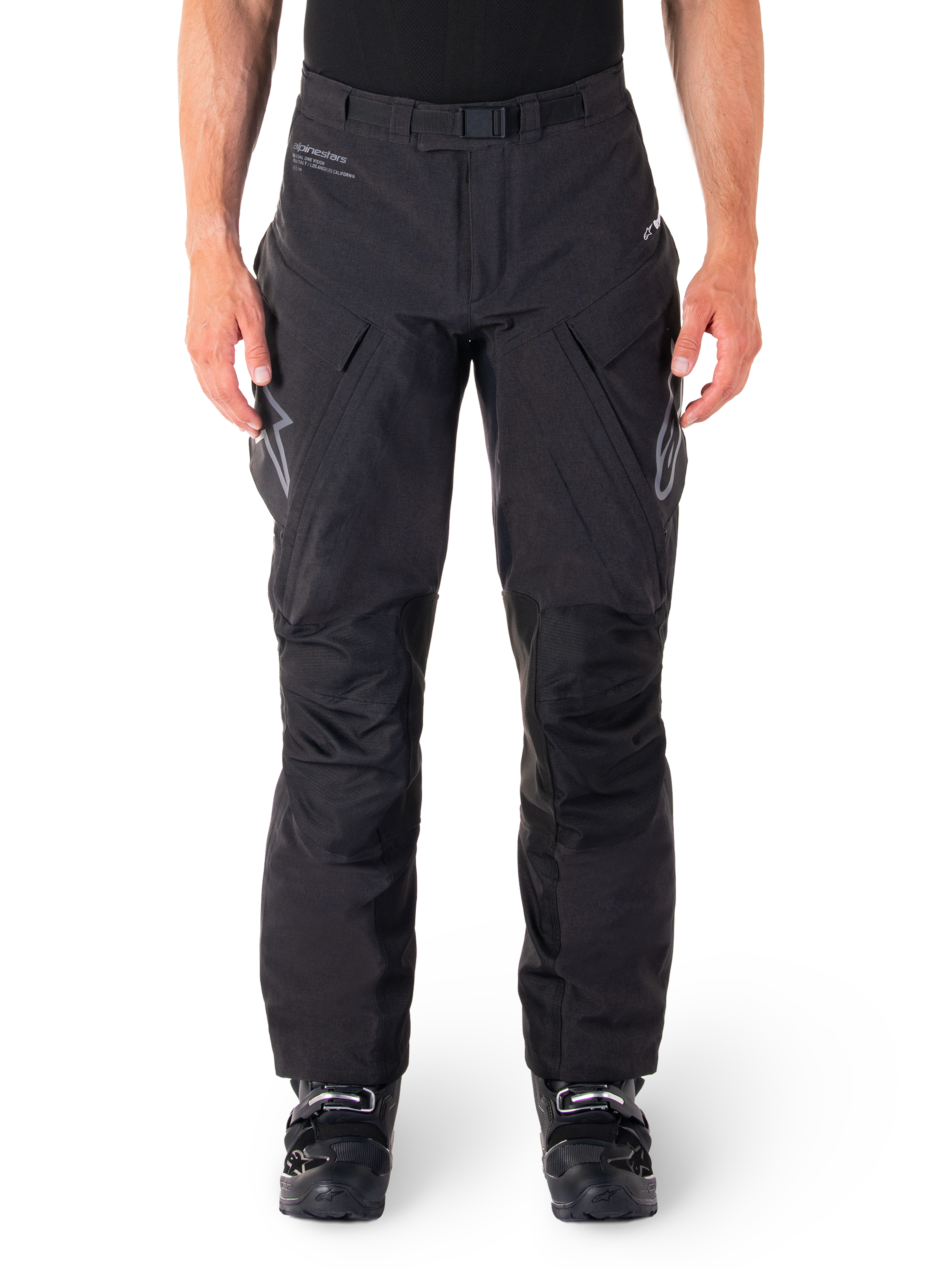 Alpinestars Hyde XT Drystar bukser, sorte adventure touring-bukser, båret af en kører med sorte støvler, med grå logoer på lårene, integreret bælte, forstærkede knæpaneler og vandtæt tekstilkonstruktion.