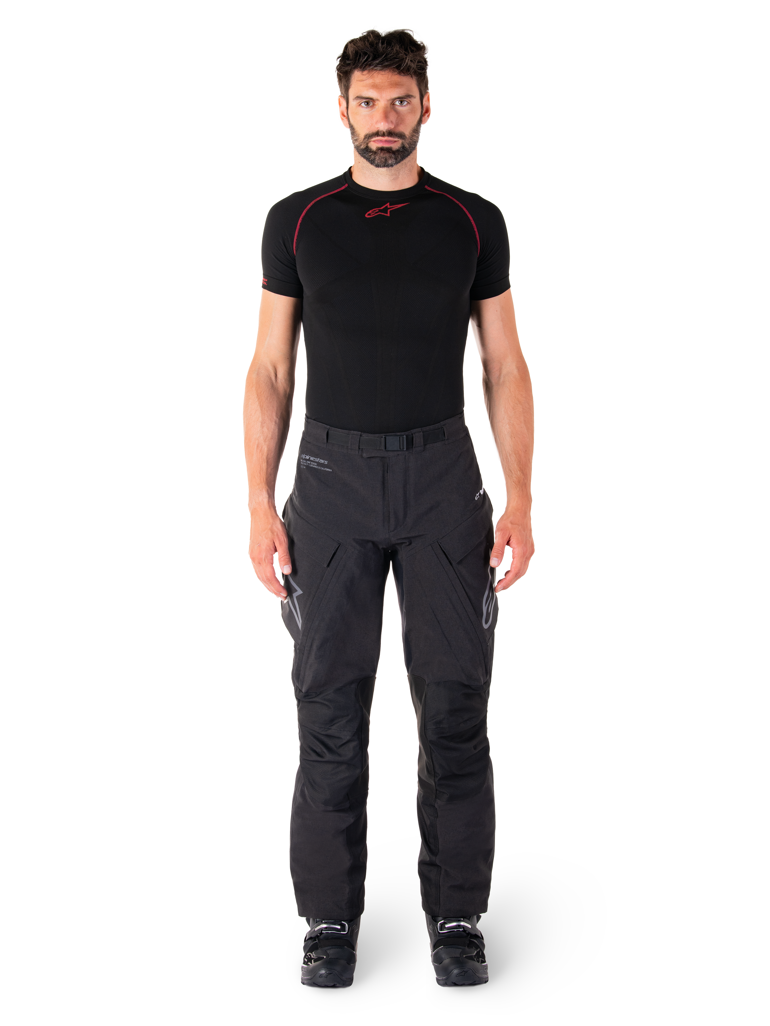 Alpinestars Hyde XT Drystar® bukser, Adventure Touring motorcykelbukser, sort, båret af en model med et sort kortærmet basislag og sorte støvler, med teknisk strækmateriale, forstærkede knæpaneler og ergonomiske cargolommer