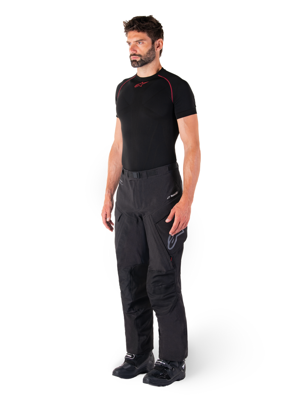 Alpinestars Hyde XT Drystar® bukser, sorte adventure touring-motorcykelbukser båret af en model med en sort kompressionstrøje og sorte støvler, med teknisk vandtæt konstruktion og Drystar®XF-branding.