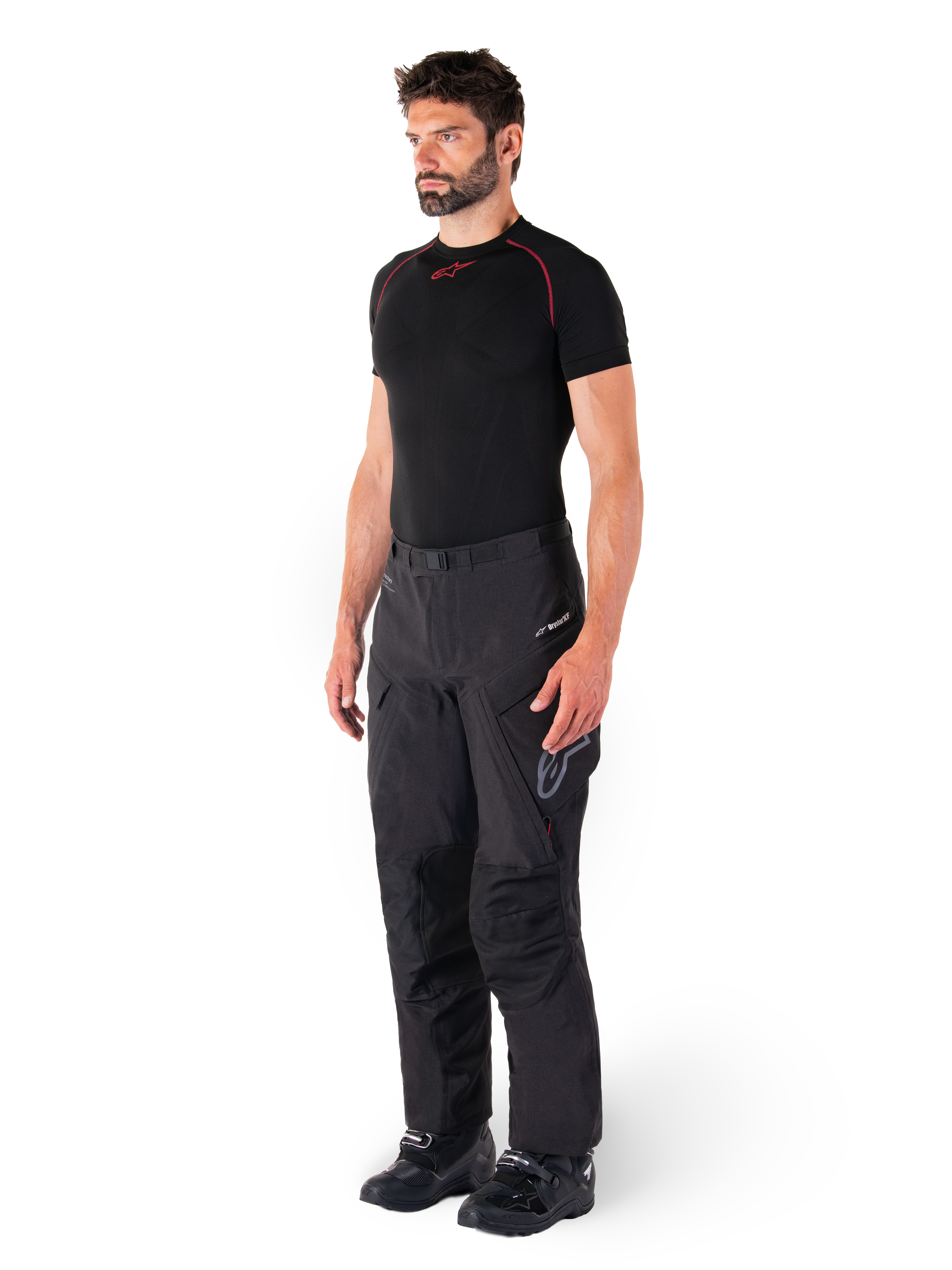 Alpinestars Hyde XT Drystar® bukser, sorte adventure touring-motorcykelbukser båret af en model med en sort kompressionstrøje og sorte støvler, med teknisk vandtæt konstruktion og Drystar®XF-branding.