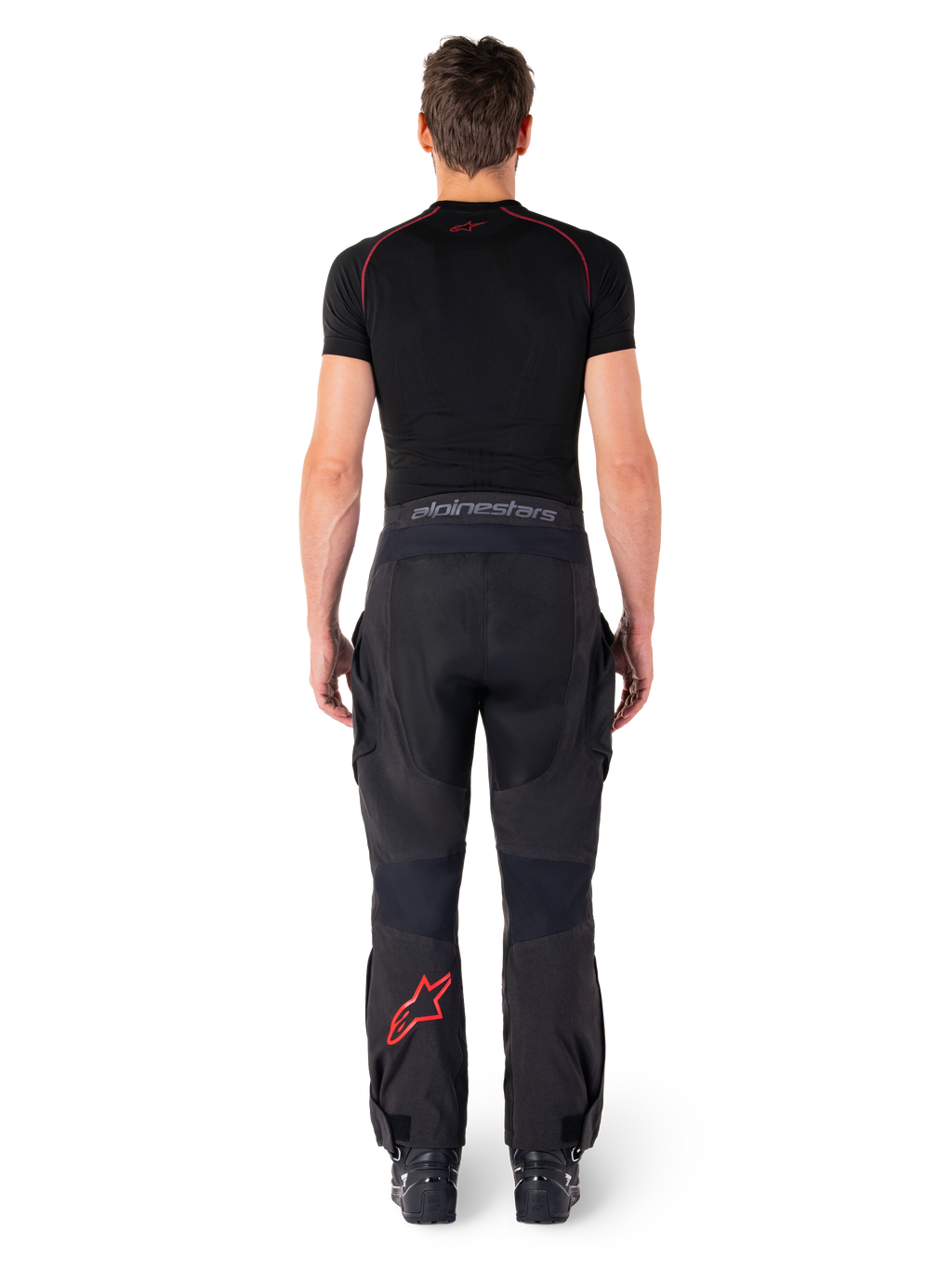 Alpinestars Hyde Xt Drystar® bukser, adventure touring motorcykelbukser, sort og lysende rød, set bagfra af en rytter iført bukserne og et sort basislag, med et rødt stjernelogo på venstre ben og gråt branding på taljebåndet.