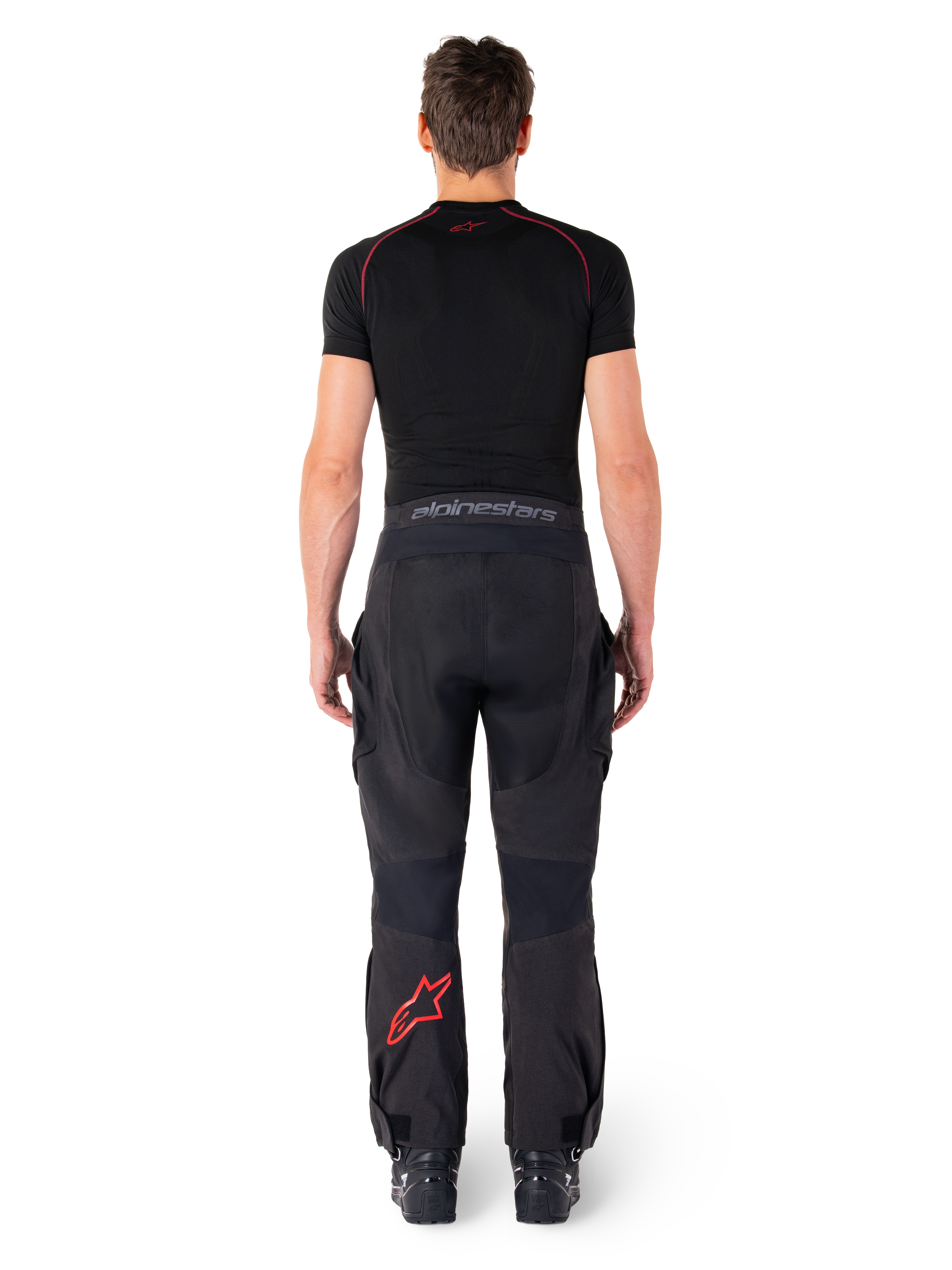 Alpinestars Hyde Xt Drystar® bukser, adventure touring motorcykelbukser, sort og lysende rød, set bagfra af en rytter iført bukserne og et sort basislag, med et rødt stjernelogo på venstre ben og gråt branding på taljebåndet.