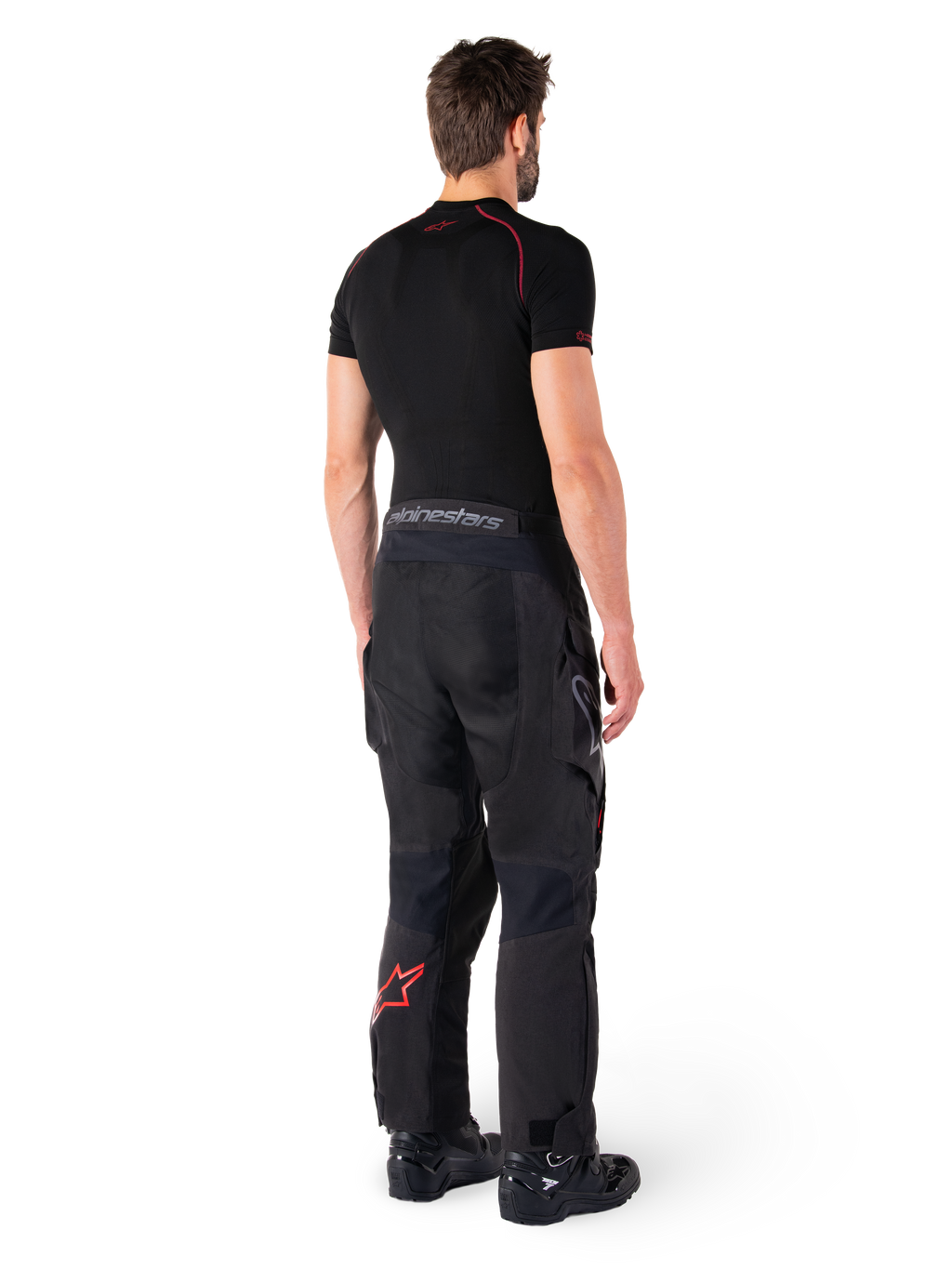 Alpinestars Hyde XT Drystar® bukser, adventure touring-bukser, sort og klar rød, set bagfra af en kører iført bukserne med et sort basislag og sorte støvler, slidstærk tekstilkonstruktion med et rødt stjernelogo på underbenet og grå Alpinestars-branding på linningen