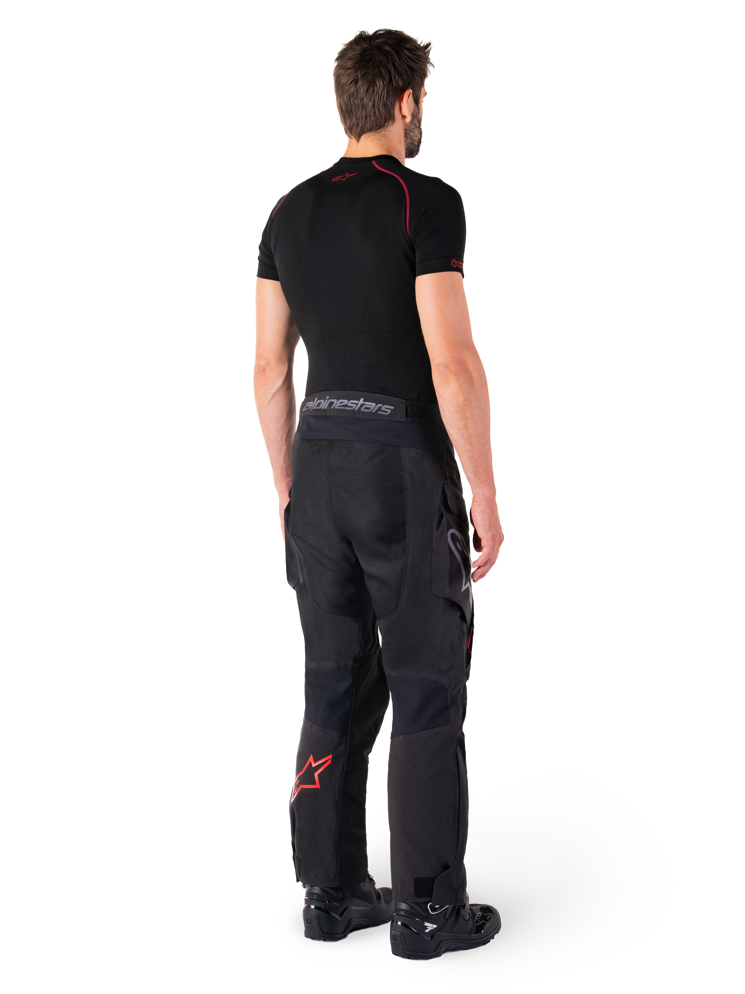 Alpinestars Hyde XT Drystar® bukser, adventure touring-bukser, sort og klar rød, set bagfra af en kører iført bukserne med et sort basislag og sorte støvler, slidstærk tekstilkonstruktion med et rødt stjernelogo på underbenet og grå Alpinestars-branding på linningen