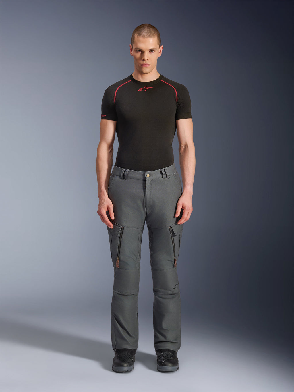 Alpinestars Borrego Drystar® bukser, grå adventure motorcykelbukser, båret af en model med en sort og rød teknisk t-shirt og sorte støvler, cargolommer med lodrette lynlåse, robust voksbehandlet lærredsudseende, slidstærkt design til adventure touring og landevejskørsel