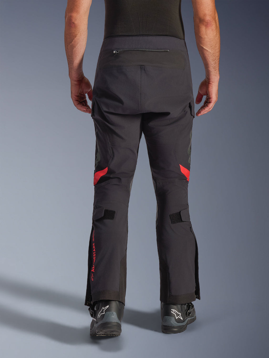 Alpinestars Halo Pro Drystar® XF laminerede bukser, Black Dark Shadow, set bagfra af adventure-motorcykelbukser med røde detaljer bag knæene og rødt logo på læggen, bæres med sorte Alpinestars-støvler, holdbart 3L lamineret tekstil til præstation i alle terræner