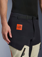 Alpinestars Halo Pro Drystar® XF laminerede bukser, adventure motorcykelbukser, Mastic Black og beige, nærbillede der viser den orange 'ALL TERRA' logopatch, sort justerbart taljebælte, slidstærkt teknisk stof med vandtætte lynlåse.