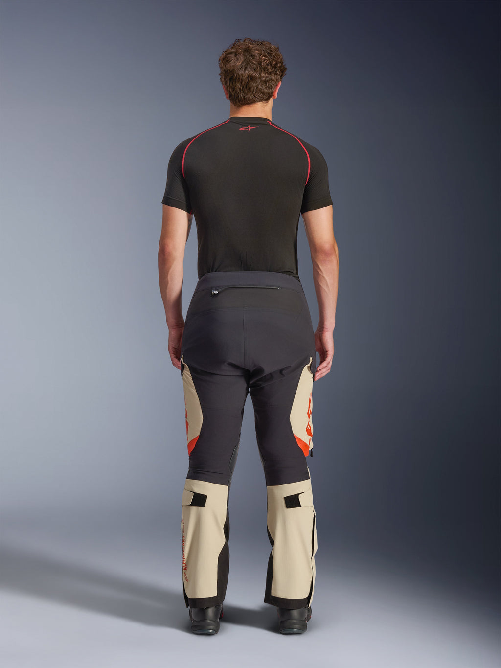 Alpinestars Halo Pro Drystar® XF laminerede bukser, Mastic Black, set bagfra på en model, sort og beige farveblokering med orange logoer, adventure motorcykel touringbukser med holdbar tekstilkonstruktion og justerbare lægsektioner
