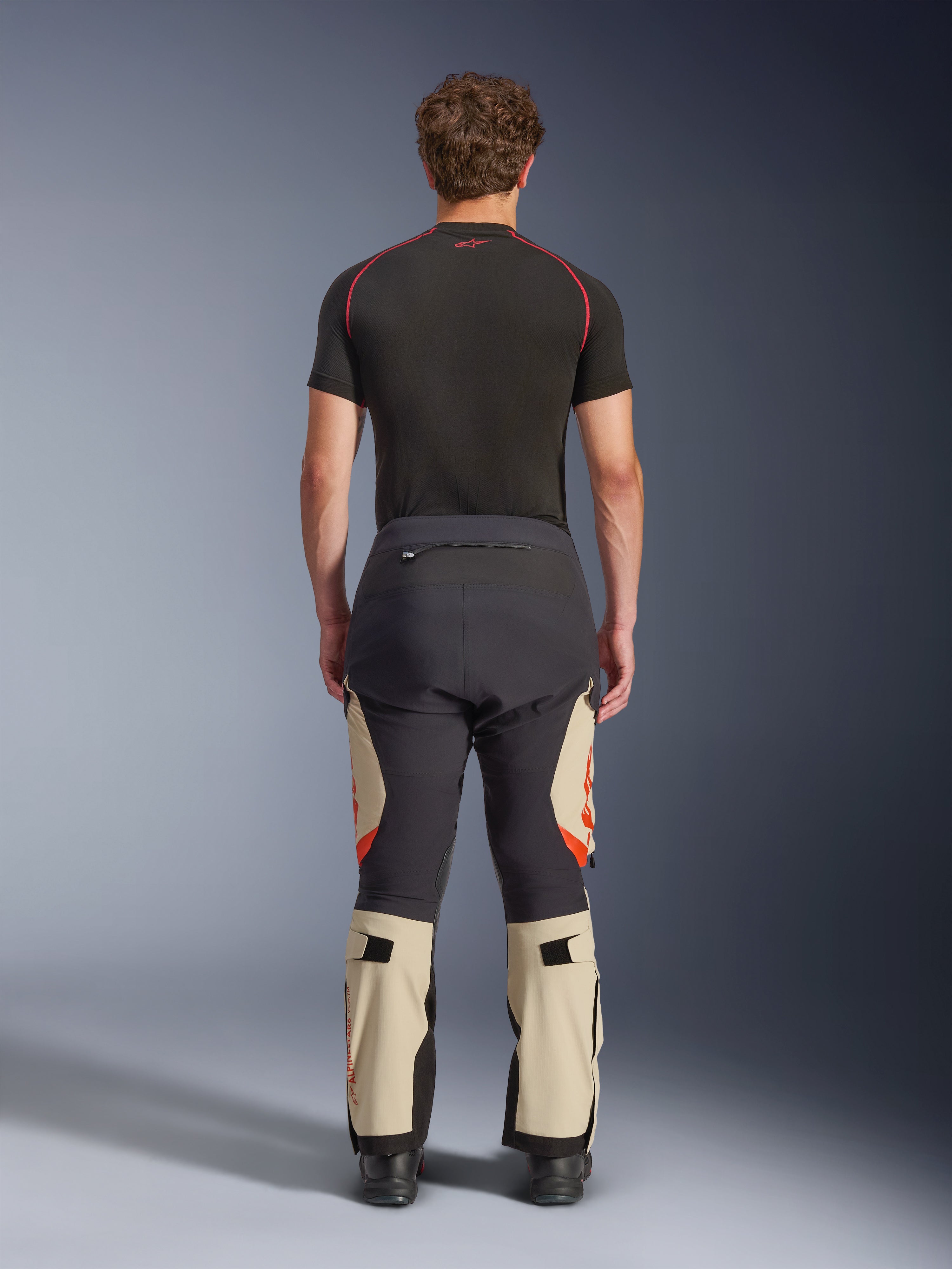 Alpinestars Halo Pro Drystar® XF laminerede bukser, Mastic Black, set bagfra på en model, sort og beige farveblokering med orange logoer, adventure motorcykel touringbukser med holdbar tekstilkonstruktion og justerbare lægsektioner