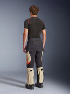 Alpinestars Halo Pro Drystar® XF laminerede bukser, adventure-motorcykelbukser, Mastic Black og Tan med orange detaljer, set bagfra viser 3-lags lamineret skalkonstruktion, kombineret med et sort basislag og adventure-støvler.