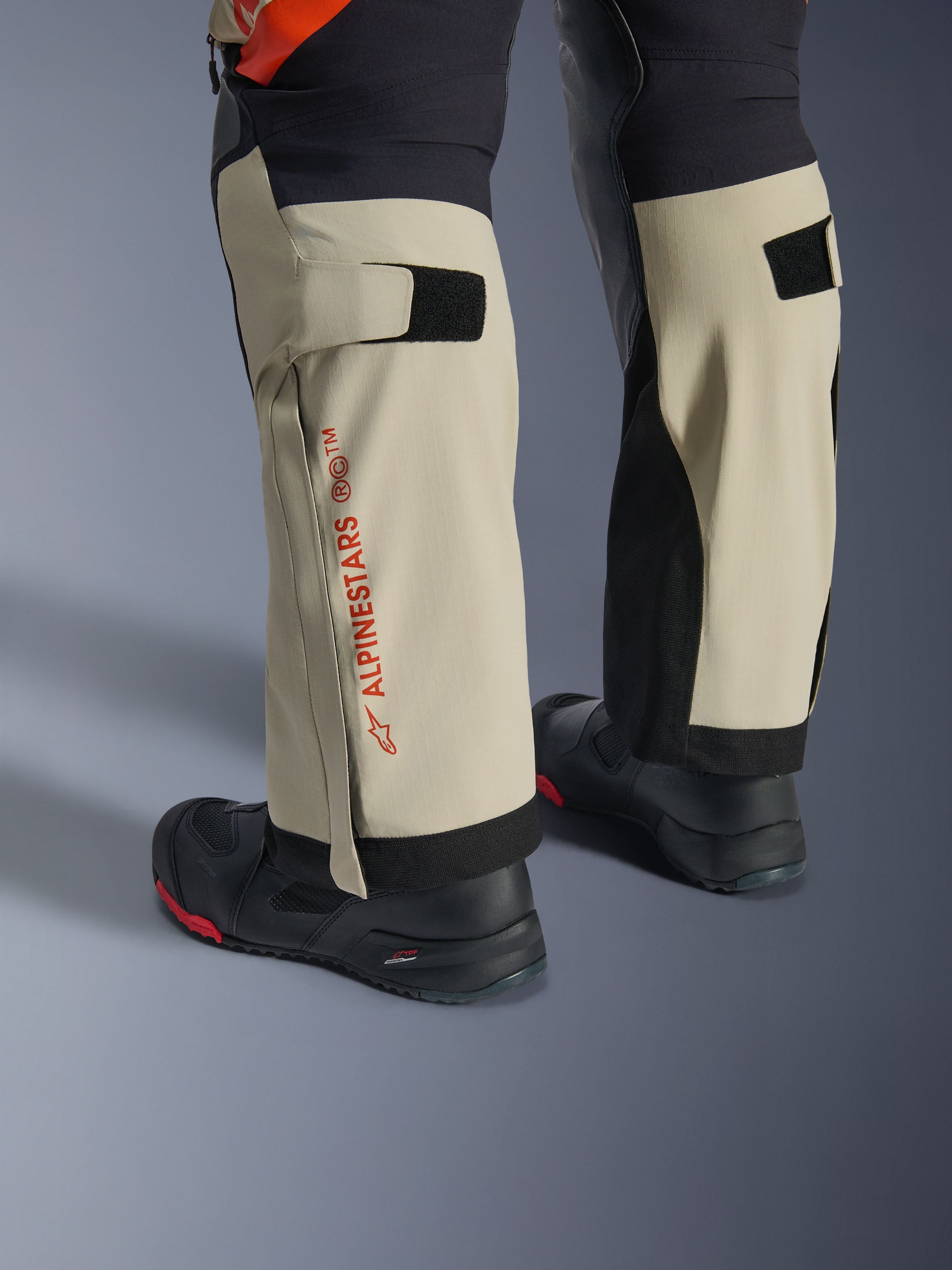 Alpinestars Halo Pro Drystar® XF laminerede bukser, Mastic Black, nærbillede af underbenene med rødt Alpinestars-branding og velcro-lægjusteringer, båret med sorte adventure-støvler