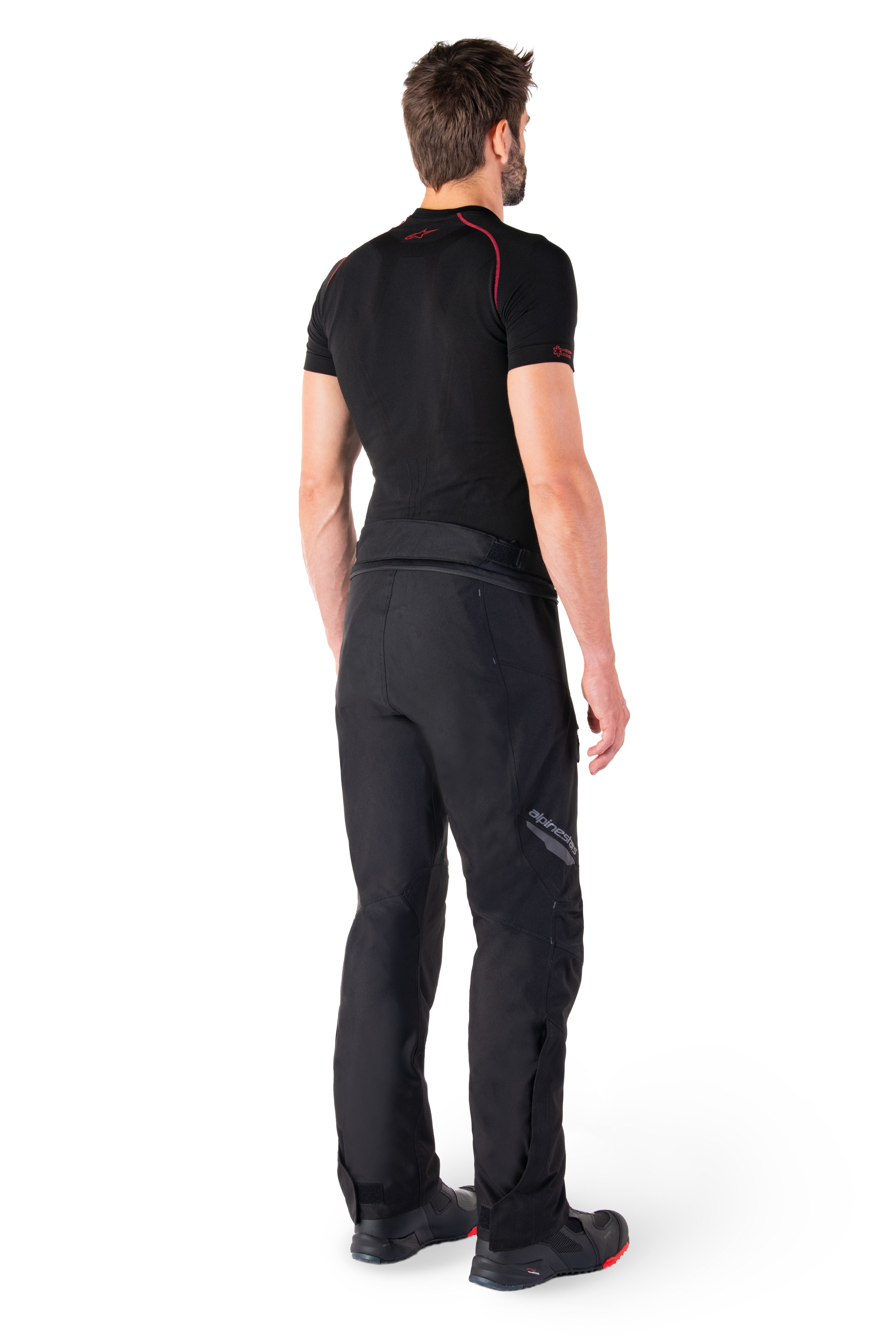 Alpinestars St-1 Waterproof Pants, Black motorcycle touring pants, three-quarter rear view on a model wearing a black base layer and black riding boots, featuring reflective Alpinestars branding on the thigh and a streamlined ergonomic design.