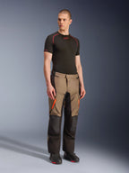 Alpinestars Andes V4 Drystar® bukser, adventure touring-bukser til motorcykel, Walnut Black med orange detaljer, vist på model med sort kortærmet baselayer og sorte støvler, med forstærkede tekstilpaneler og cargolommer, robust design til kørsel i al slags vejr