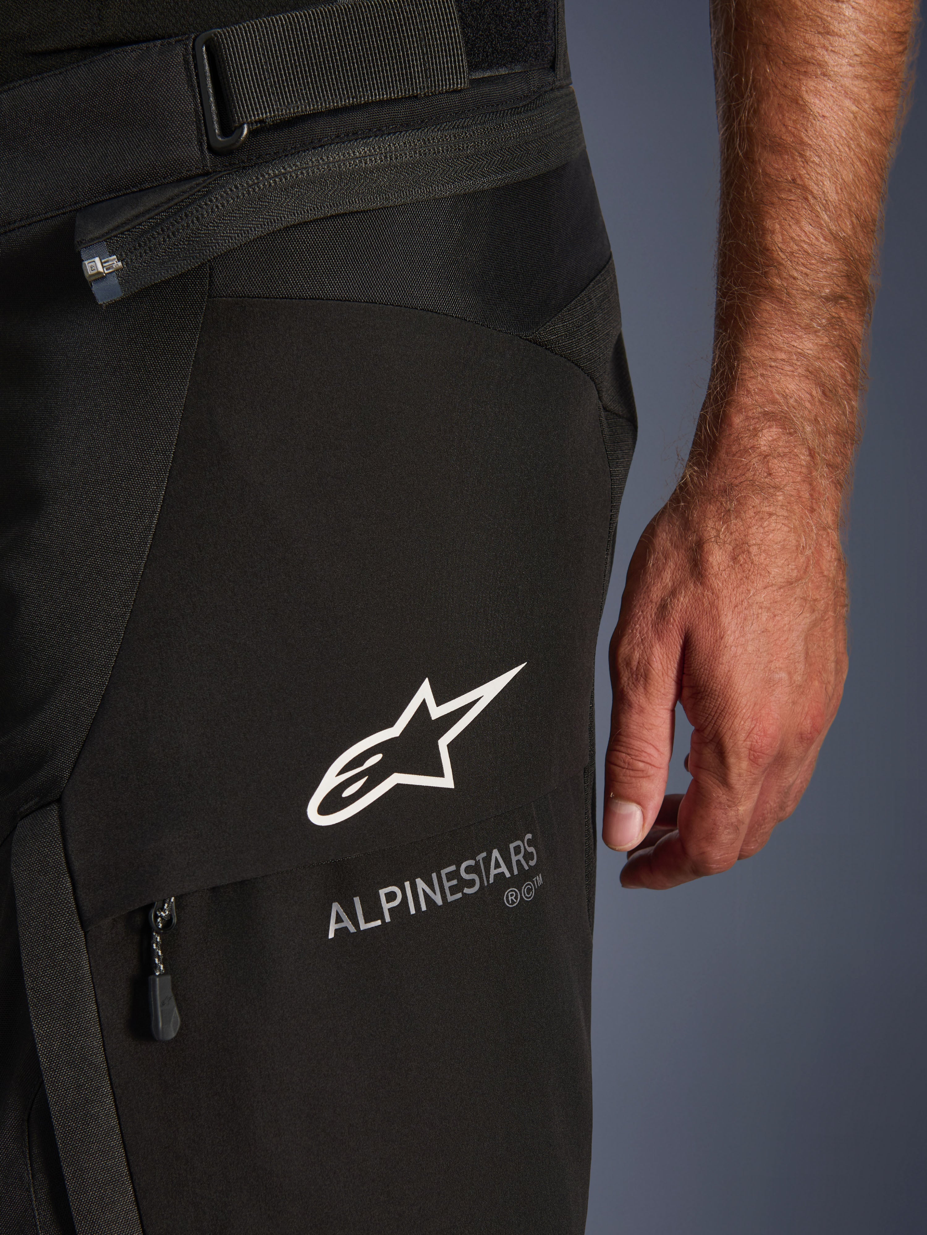 Nærbillede af Alpinestars Andes V4 Drystar® bukser i sort, med hvidt Alpinestars-logo og navnetræk på en cargolomme, synlig justeringsrem i taljen og forbindelseslynlås, designet til adventure-motorcykelkørsel.