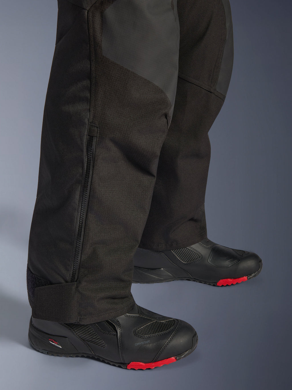 Alpinestars Andes V4 Drystar® bukser - Short, sort, nærbillede af detalje på underbenet, der viser tekstilkonstruktion, lodret lynlås til ventilation og justerbare ankelmanchetter, båret med sorte motorcykelstøvler