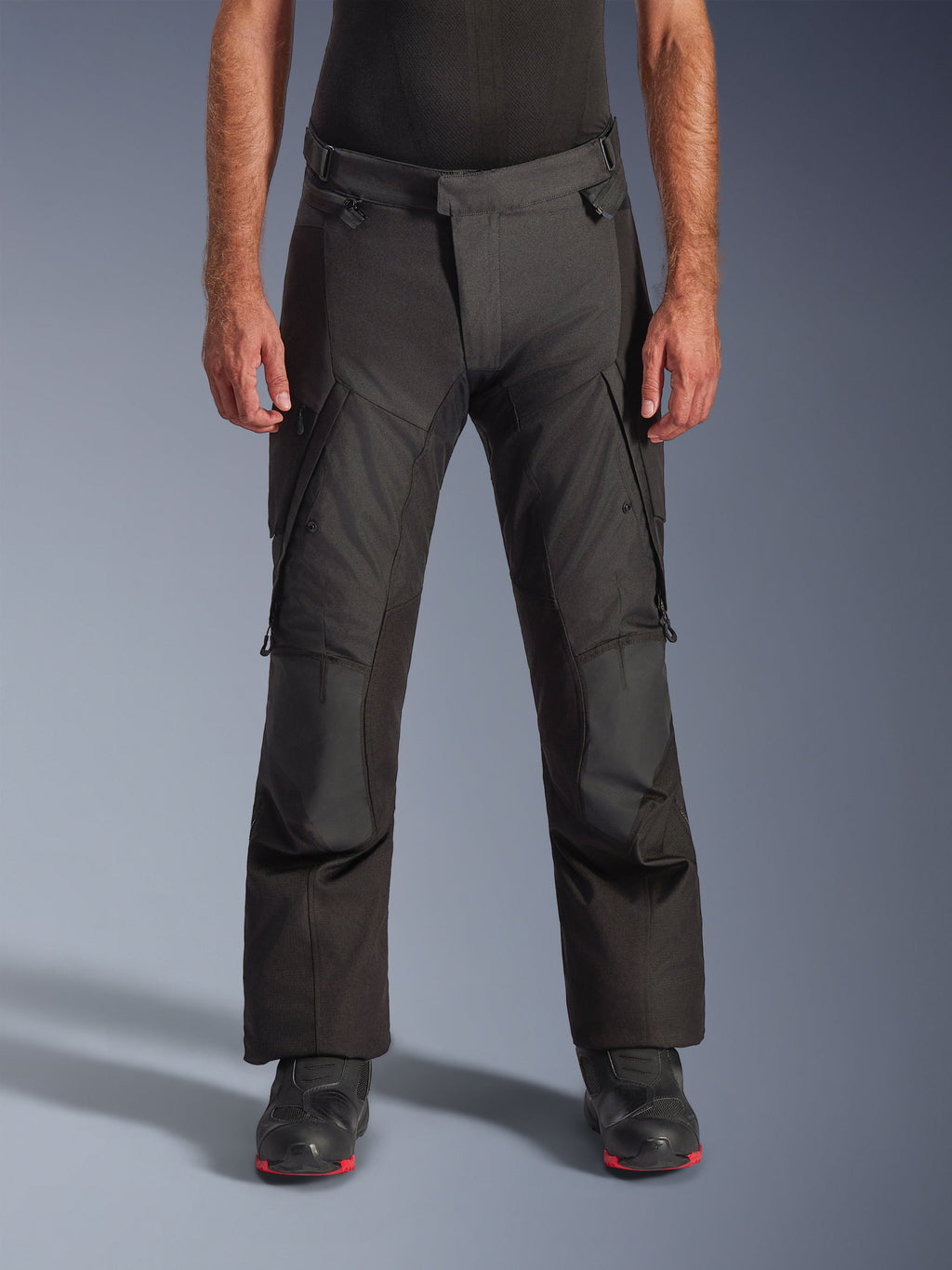 Alpinestars Andes V4 Drystar bukser, adventure touring-motorcykelbukser, sorte med grå paneler, med forstærkede knæstykker og cargolommer på lårene, vist med sorte støvler, vandtæt tekstilkonstruktion til kørsel i al slags vejr