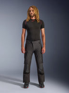 Mandlig model med langt hår iført Alpinestars Andes V4 Drystar® bukser i sort, adventure touring-motorcykelbukser med forstærkede knæpaneler og cargolommer, stylet med et sort kortærmet basislag og motorcykelstøvler.