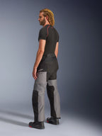 Alpinestars Andes V4 Drystar® Pants, Motorcycle Adventure Pants, Black and Dark Gray, worn with a black short-sleeved base layer and black motorcycle boots, side and back view featuring multi-panel textile design and Alpinestars branding on the thigh.
