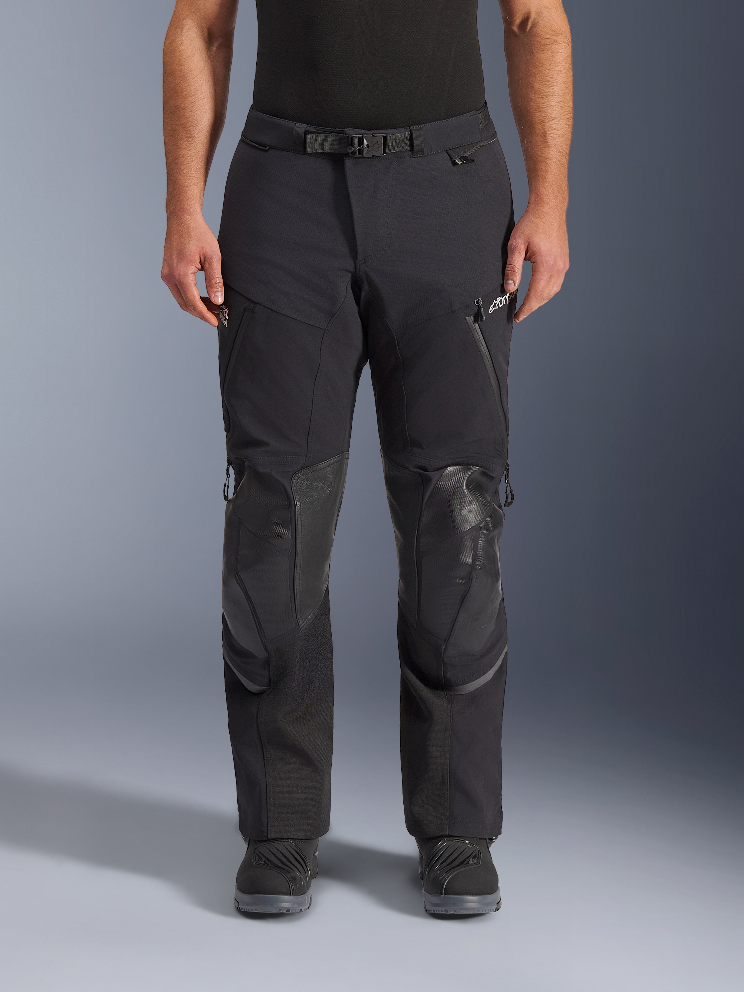 Alpinestars Andes Pro Drystar® XF bukser, sort mørkegrå adventure touring motorcykelbukser, set forfra, med 3-lags lamineret konstruktion, integrerede knæbeskyttelsespaneler, vandtætte lynlåslommer og magnetisk taljespænde, stylet med sorte mc-støvler.