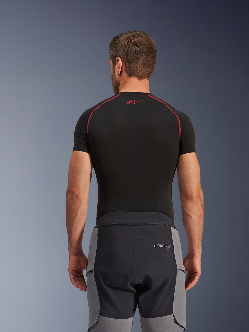 Alpinestars Andes Pro Drystar® XF bukser, adventure motorcykelbukser, mørkegrå og sort, set bagfra med visning af taljekonstruktion og grå sidepaneler, båret med en sort base layer-overdel med røde syninger, teknisk touring-udstyr til al slags vejr