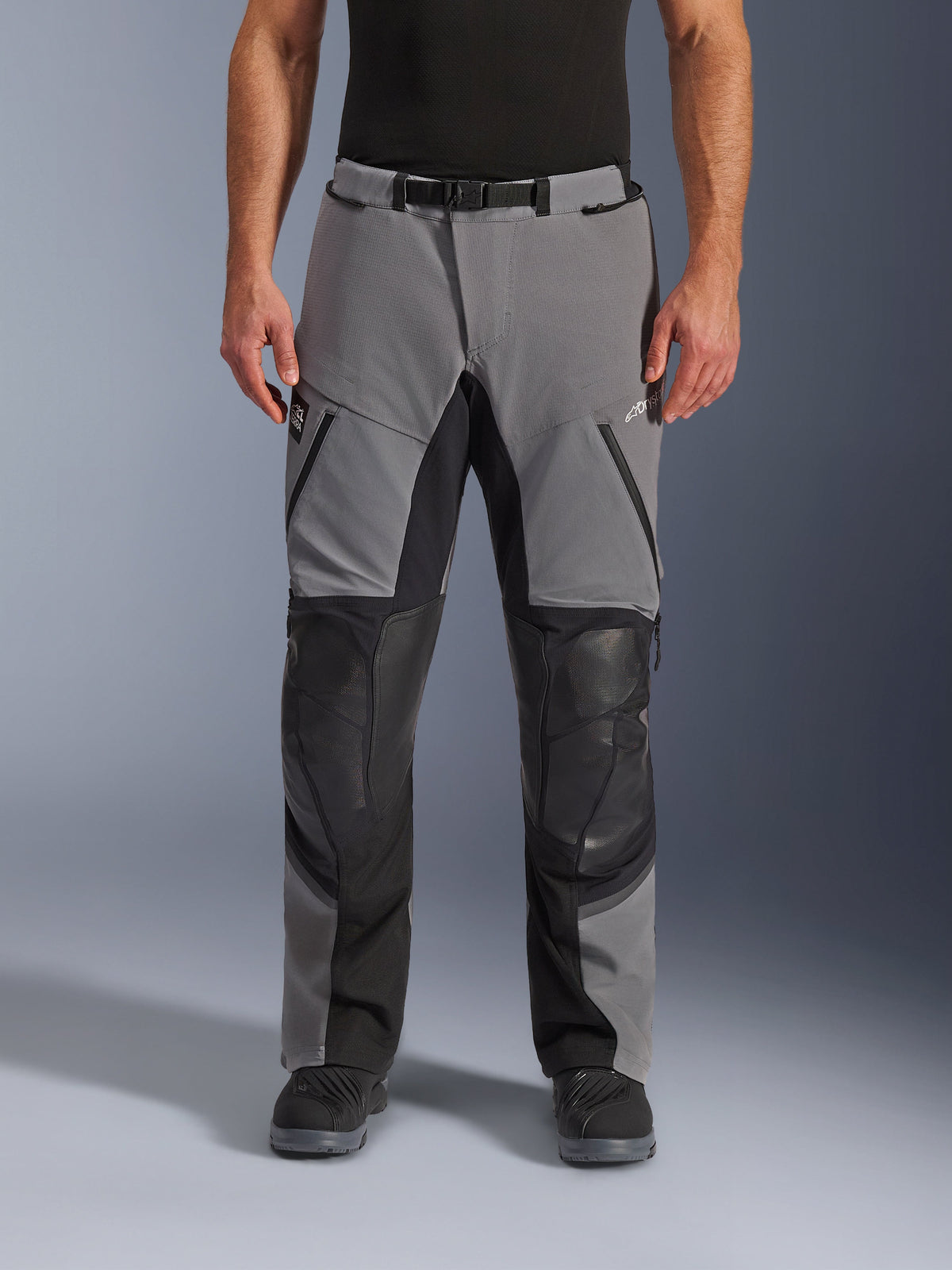 Alpinestars Andes Pro Drystar® XF bukser, motorcykelbukser, mørkegrå og sort, set forfra, med forstærkede sorte knæpaneler, vandtætte lynlåse og bælte med magnetisk spænde, båret med sorte støvler