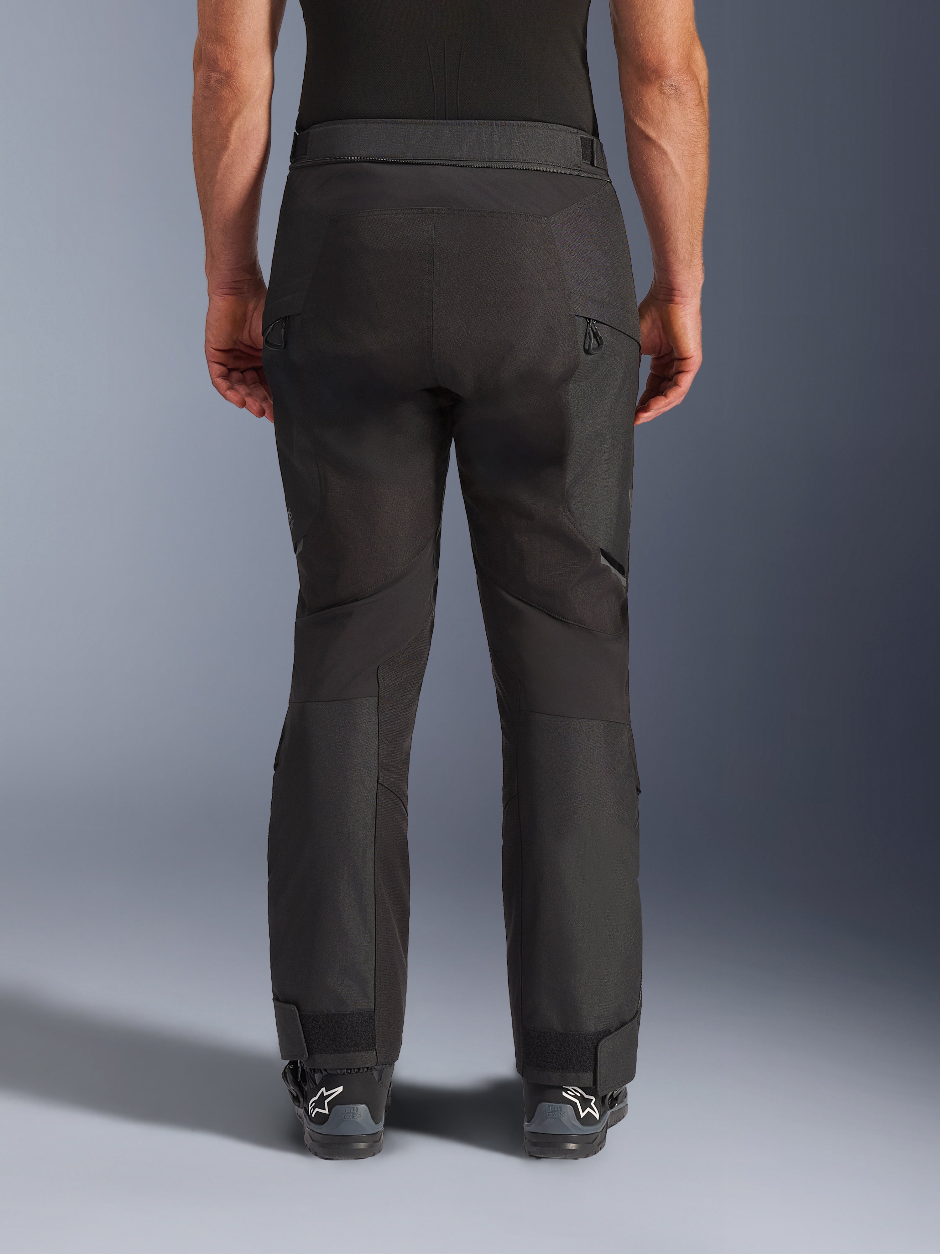 Alpinestars Cusco Drystar® bukser, motorcykelbukser, sort, set bagfra båret af en kører, med teksturerede tekstilpaneler, ventilationsåbninger med lynlås på lårene og justerbare ankellukninger, kombineret med sorte Alpinestars-støvler.