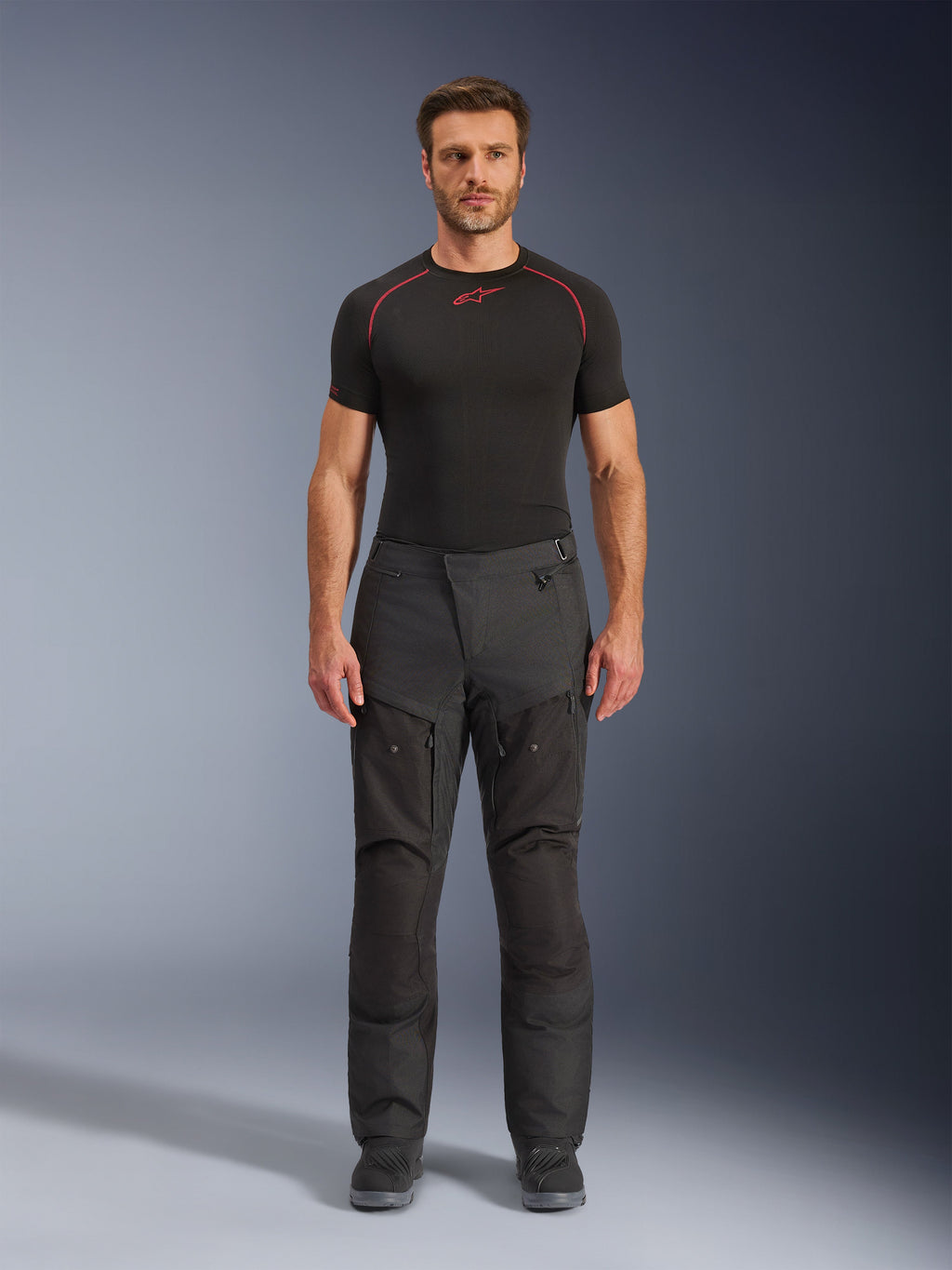 Alpinestars Cusco Drystar® bukser, tekstil motorcykelbukser, sorte, båret af en model med et sort basislag og støvler, adventure touring-design med lårventilationspaneler med lynlås og en holdbar konstruktion med flere paneler