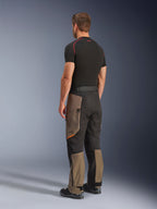 Alpinestars Cusco Drystar® bukser, adventure motorcykelbukser, Walnut Black, trekvartvisning bagfra, båret med et sort basislag og støvler, med forstærkede tekstilpaneler, cargo-lommer med lynlås på lårene og en ergonomisk touring-pasform.