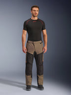 Alpinestars Cusco Drystar® bukser, Walnut Black, adventure touring motorcykelbukser, bæres af en mandlig model med sort basislag og sorte støvler, paneler i valnød og sort, orange detaljer, direkte ventilationslynlåse på lårene.