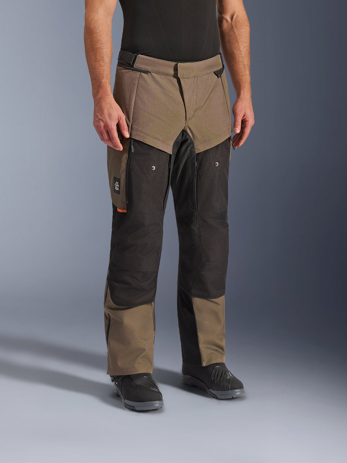 Alpinestars Cusco Drystar® bukser, adventure motorcykelbukser, Walnut Black, vist på en model med sorte støvler, med et brunt og sort multi-panel design med lynlåslommer og forstærkede knæ til touring
