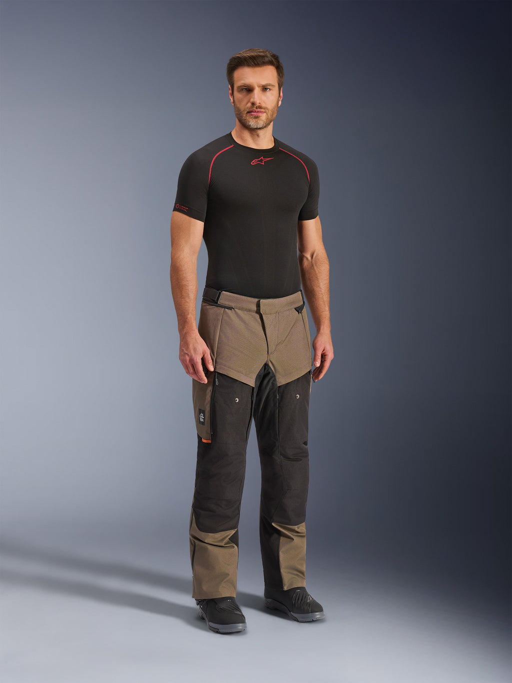 Alpinestars Cusco Drystar® bukser, adventure-motorcykelbukser, valnød og sort, båret af en model med et sort basislag og støvler, med store cargolommer på lårene, ventilationslynlåse og et robust tofarvet design.