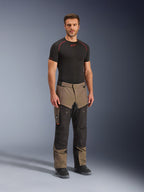 Alpinestars Cusco Drystar® bukser, adventure-motorcykelbukser, valnød og sort, båret af en model med et sort basislag og støvler, med store cargolommer på lårene, ventilationslynlåse og et robust tofarvet design.