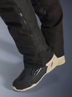 Alpinestars Stella Andes V4 Drystar® bukser, sort, nærbillede af underbenet med lynlås i siden til støvlejustering, slidstærkt tekstilmateriale, båret med sorte og sandfarvede motorcykelstøvler, adventure-klar funktionelt design