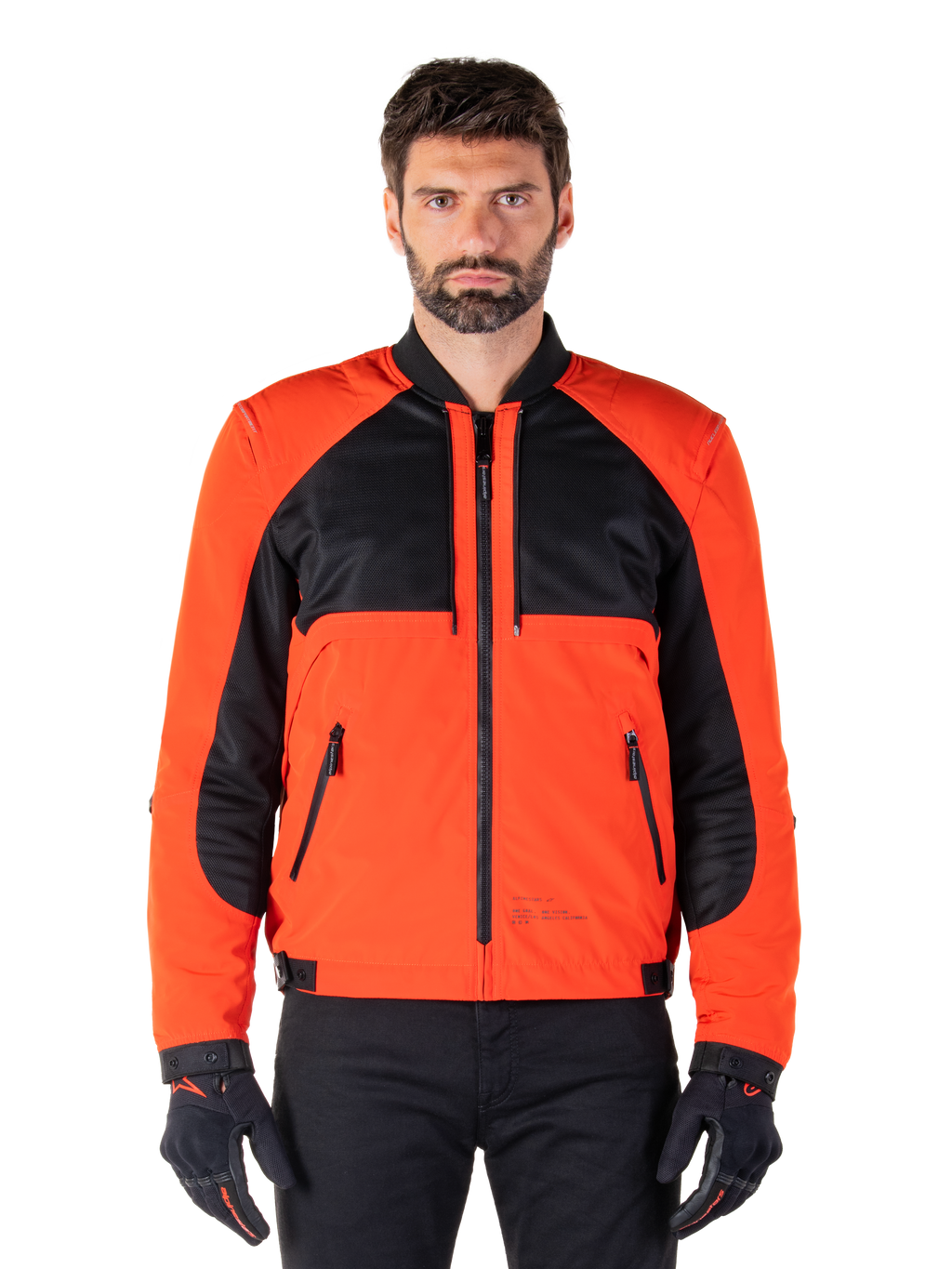 Alpinestars Mootant vandtæt parka i Spicy Orange og sort, modulær motorcykeljakke vist i en bomberjakke-konfiguration på en mandlig model, med sorte mesh-paneler på brystet, orange torso og ærmer, lynlås foran og ribbet krave, kombineret med sorte handsker og bukser