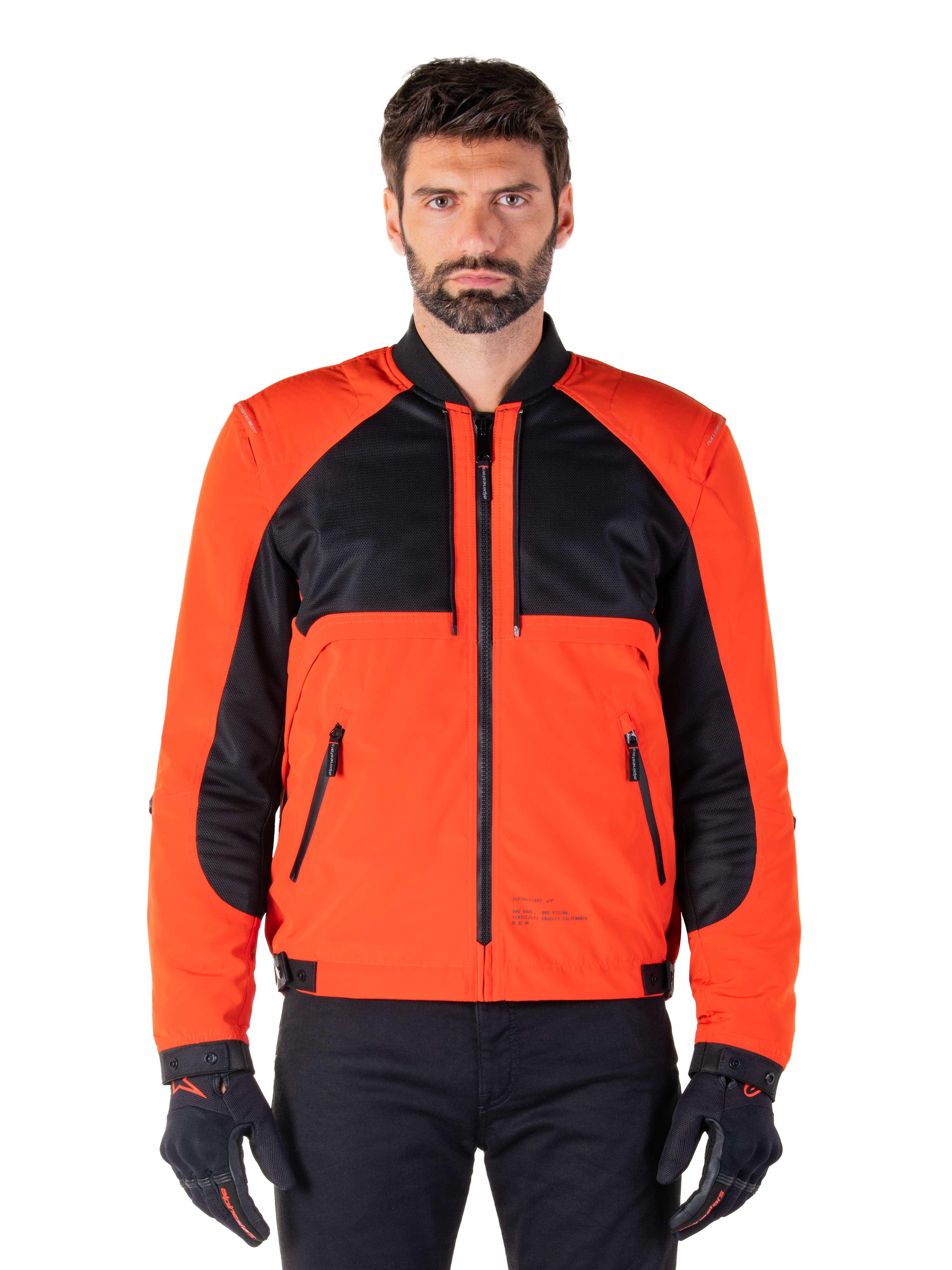 Alpinestars Mootant vandtæt parka i Spicy Orange og sort, modulær motorcykeljakke vist i en bomberjakke-konfiguration på en mandlig model, med sorte mesh-paneler på brystet, orange torso og ærmer, lynlås foran og ribbet krave, kombineret med sorte handsker og bukser