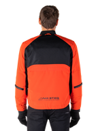 Alpinestars Mootant vandtæt parka, motorcykeljakke, Spicy Orange og sort, set bagfra, med sort mesh på den øverste del af ryggen og orange panel forneden med MO.ST.EQ.-logo, båret med sorte bukser og handsker