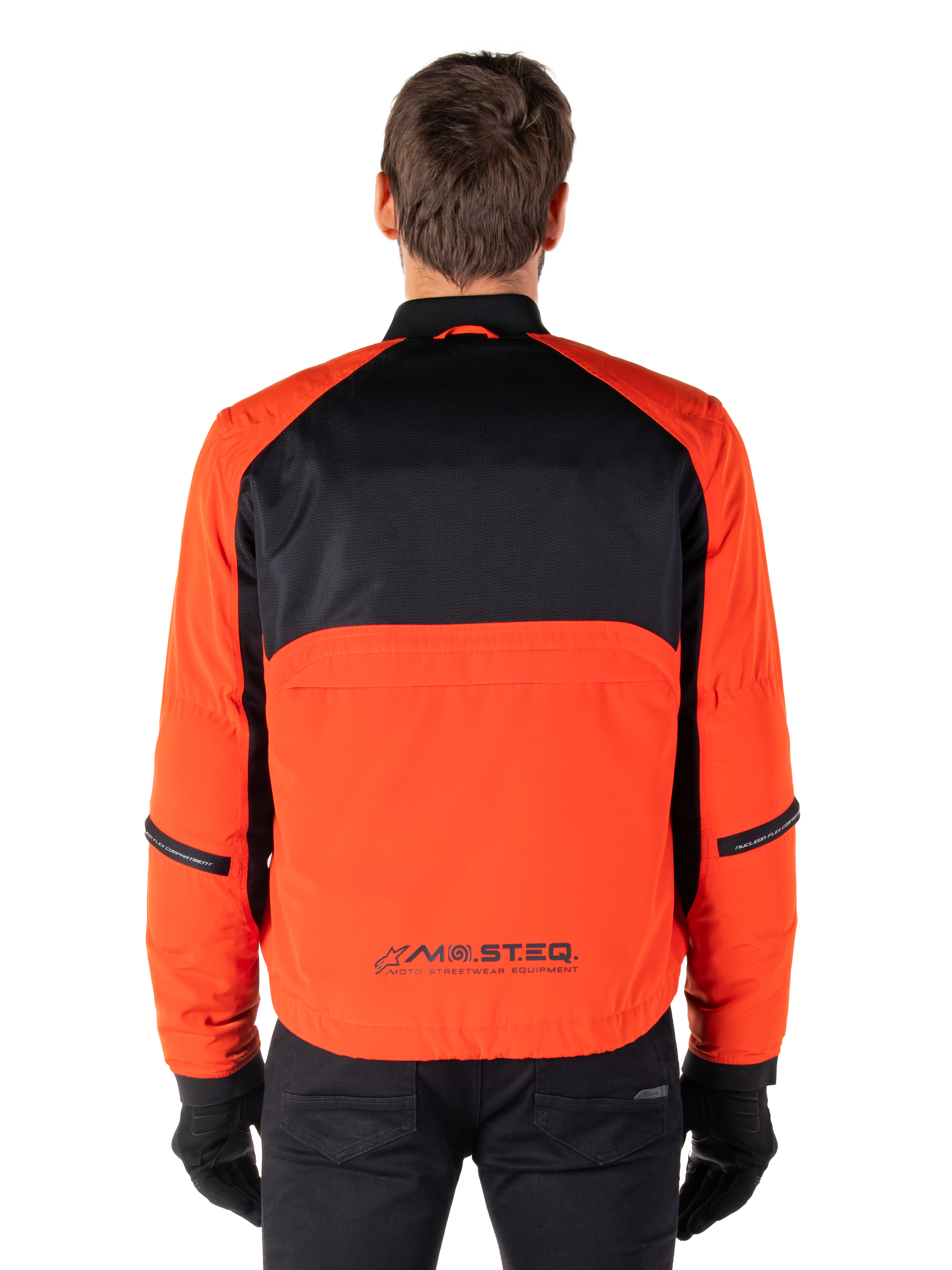 Alpinestars Mootant vandtæt parka, motorcykeljakke, Spicy Orange og sort, set bagfra, med sort mesh på den øverste del af ryggen og orange panel forneden med MO.ST.EQ.-logo, båret med sorte bukser og handsker