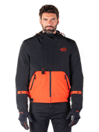 Alpinestars Mootant Waterproof Parka, modulær motorcykeljakke i Spicy Orange og sort, båret af en model med matchende handsker, design med hætte og tofarvede paneler, lynlås foran og justerbare manchetter, moderne urbant køreudstyr