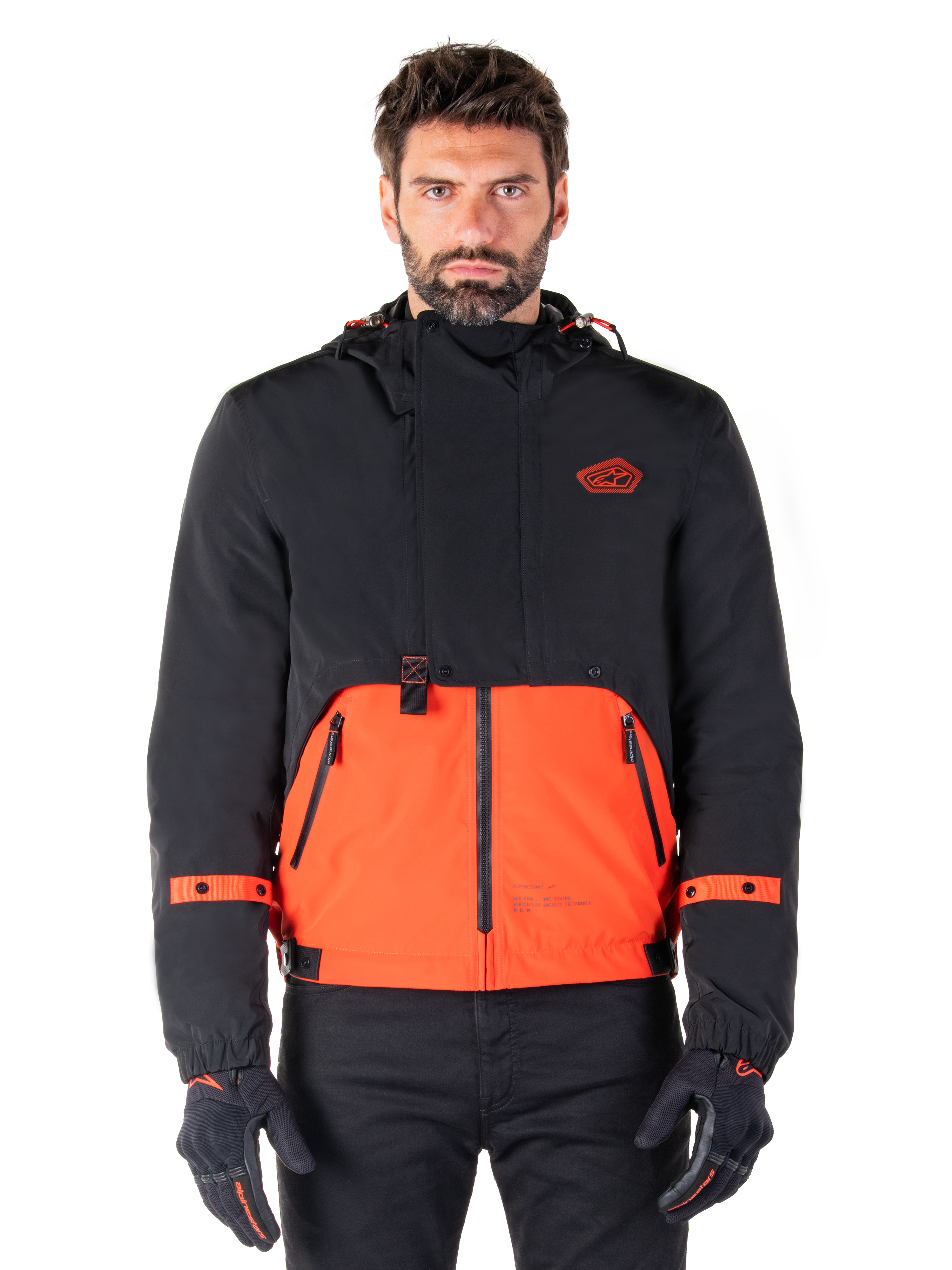 Alpinestars Mootant Waterproof Parka, modulær motorcykeljakke i Spicy Orange og sort, båret af en model med matchende handsker, design med hætte og tofarvede paneler, lynlås foran og justerbare manchetter, moderne urbant køreudstyr