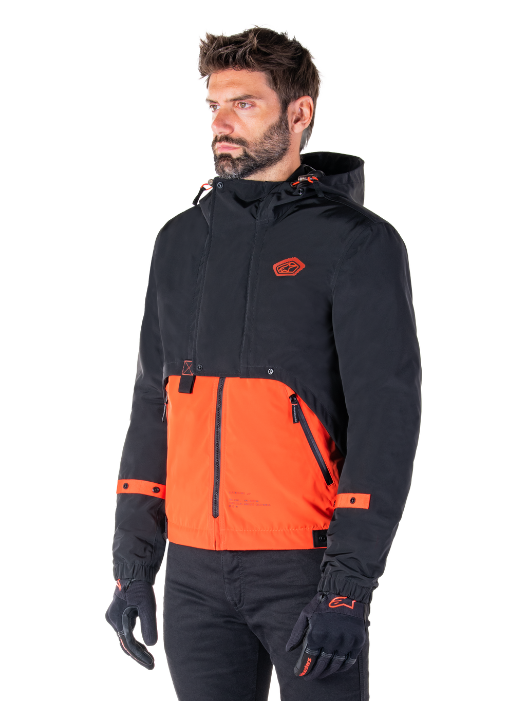 Mand iført Alpinestars Mootant Waterproof Parka i Spicy Orange og sort, en modulær motorcykeljakke med et sort øvre lag med hætte og en klar orange nedre del, stylet med sorte kørehandsker og bukser.