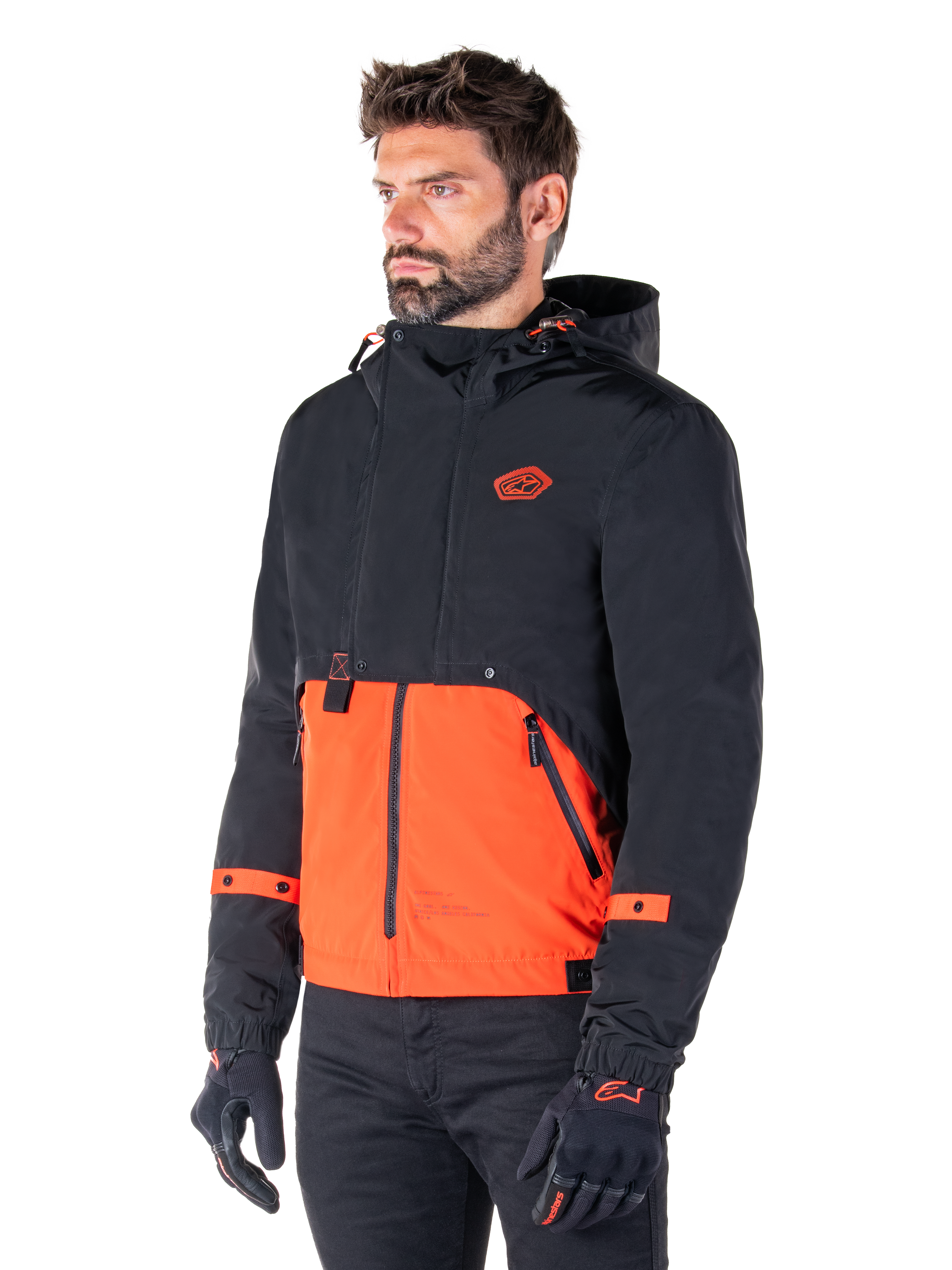 Mand iført Alpinestars Mootant Waterproof Parka i Spicy Orange og sort, en modulær motorcykeljakke med et sort øvre lag med hætte og en klar orange nedre del, stylet med sorte kørehandsker og bukser.