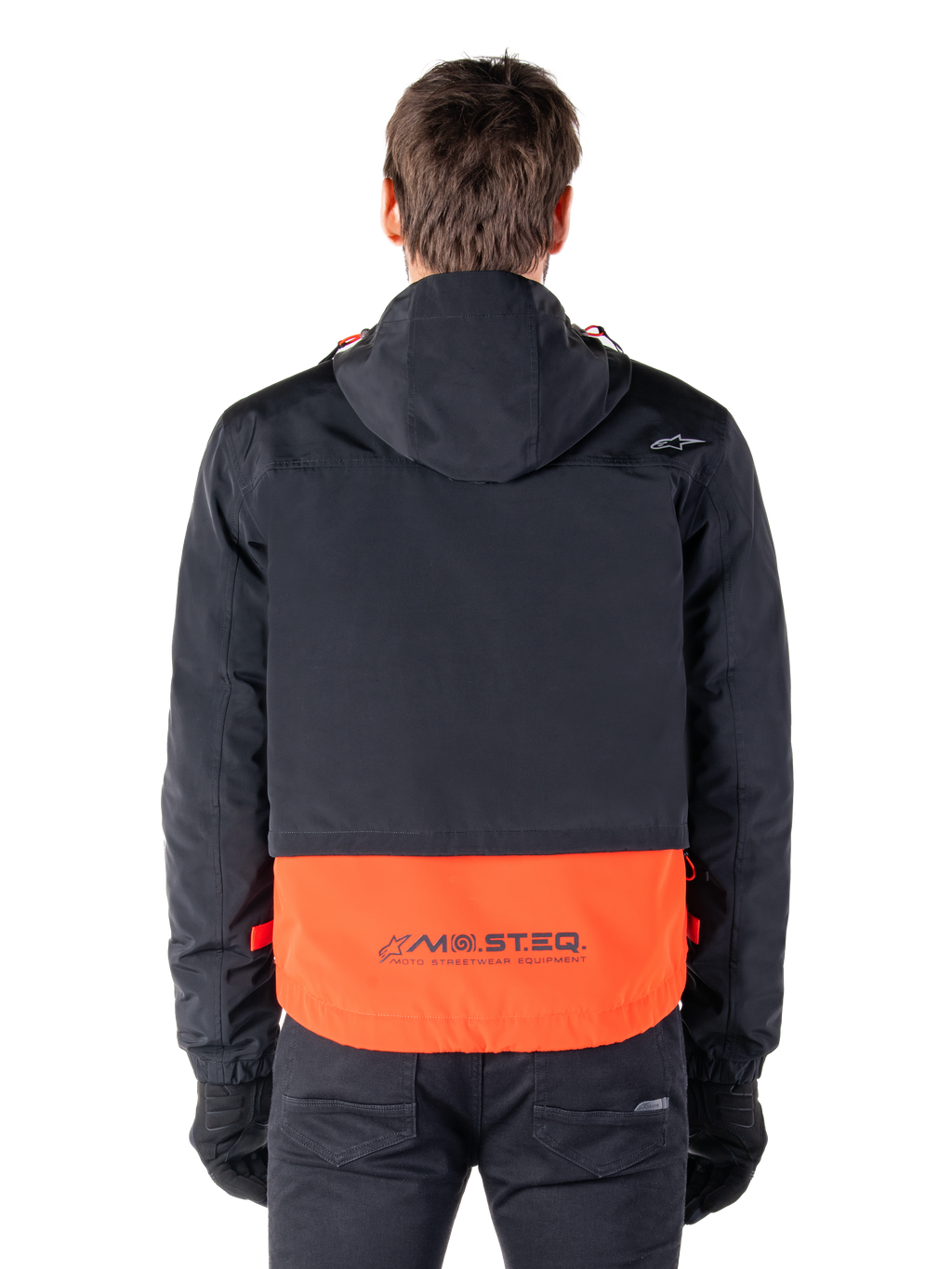 Alpinestars Mootant vandtæt parka i Spicy Orange og sort, set bagfra, viser sort overdel med hætte og orange underpanel med MO.ST.EQ.-ordmærket, funktionelt motorcykel-streetwear.
