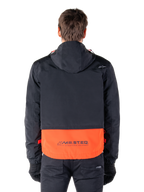 Alpinestars Mootant vandtæt parka i Spicy Orange og sort, set bagfra, viser sort overdel med hætte og orange underpanel med MO.ST.EQ.-ordmærket, funktionelt motorcykel-streetwear.